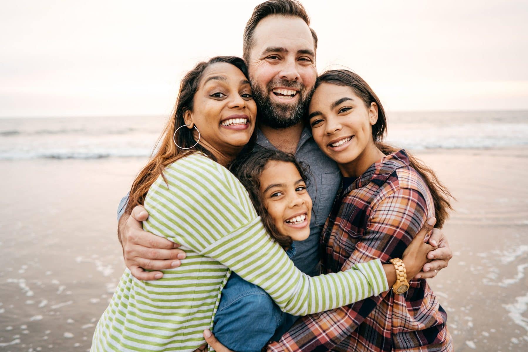 A missionary family of 4 in a group hug by the beach