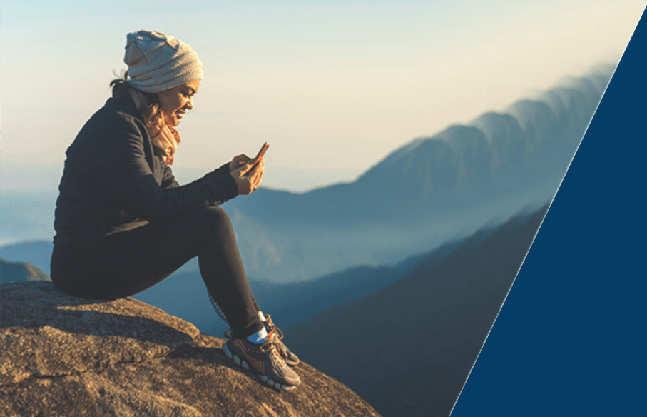 A woman sitting on a mountain looking at her phone wondering if she has health insurance