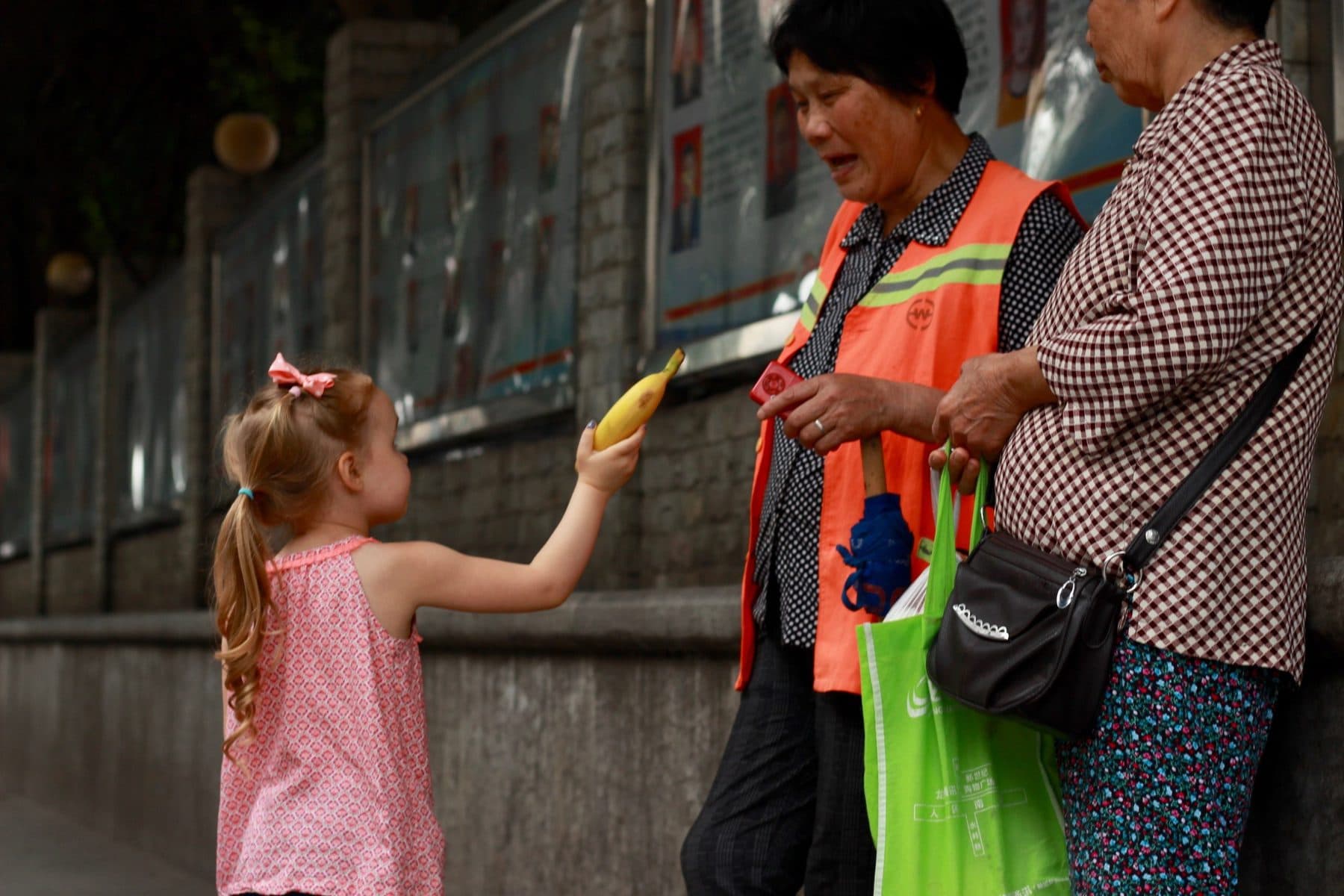 A missionary's young child gives a banana to two older ladies on the street